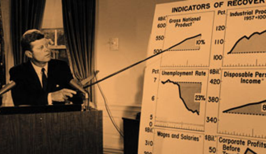 John F. Kennedy points to a series of graphs