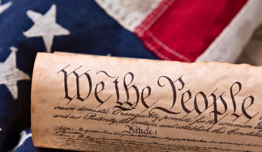 Constitution rolled up with American flag behind it.